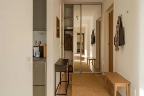En hall med en träbänk, en smal konsol och en stor spegelgarderob. Hållbar inredning med naturliga material som jute och trä.