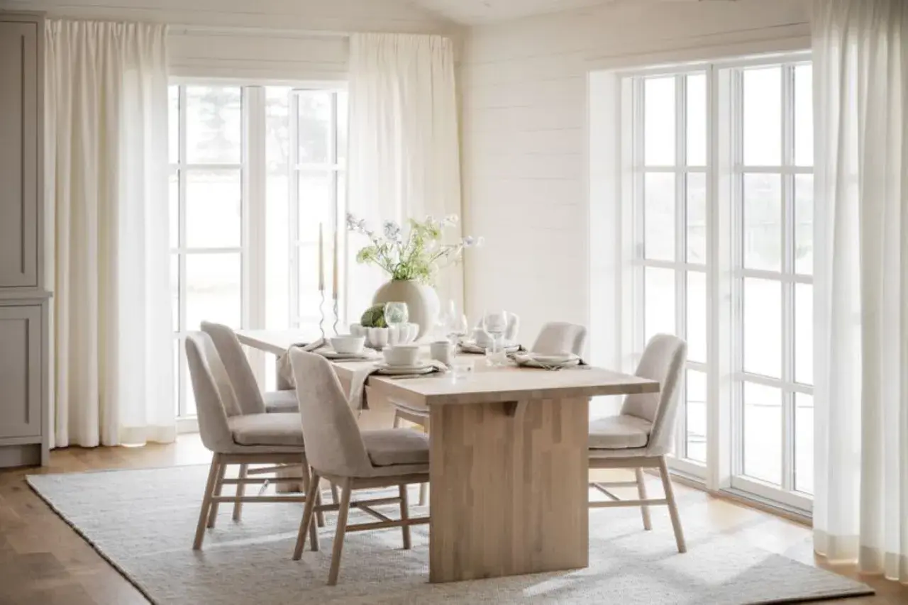Ljus och luftig matplats med inspiration från naturen. Träbord, beiga stolar och stora fönster med vita gardiner skapar en harmonisk känsla.