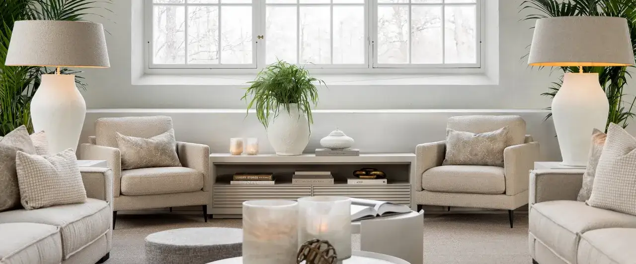 En ljus och luftig lounge med bekväma fåtöljer i Newport-stil, prydda med dekorativa kuddar. En stor grön växt och stilrena lampor skapar en harmonisk atmosfär.