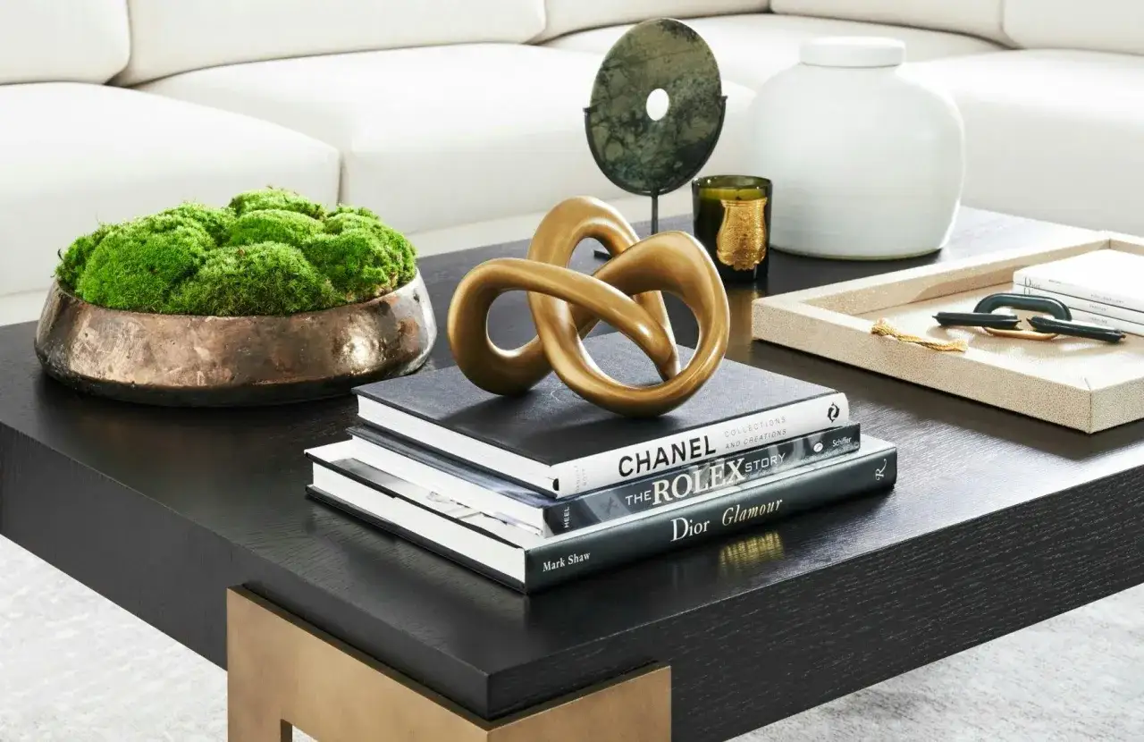 Soffbord med konstverk, böcker om Chanel, Rolex och Dior, samt en mosskål. En perfekt inspiration för att styla soffbord.