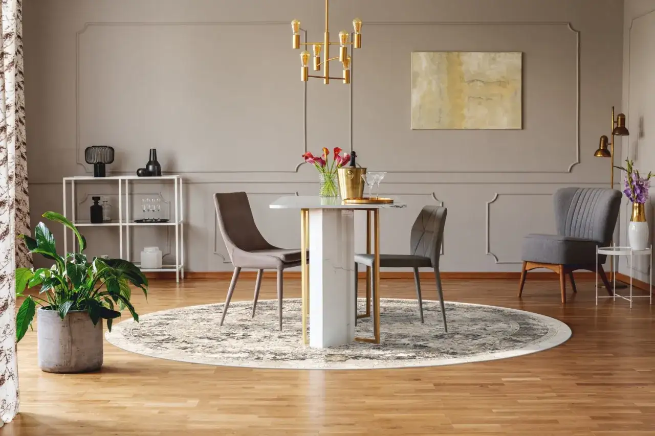 En rund matta under ett elegant runt matbord med två stolar. En guldig taklampa lyser upp rummet.