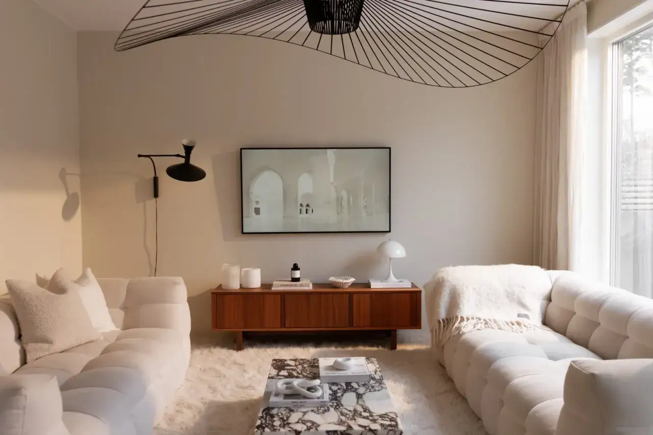 Mysigt vardagsrum med vita soffor, marmorbord och en tv-b&auml;nk i teak. Tv&aring; vita ljus p&aring; b&auml;nken bidrar till en ombonad k&auml;nsla, perfekt f&ouml;r ett diy ljus-projekt.