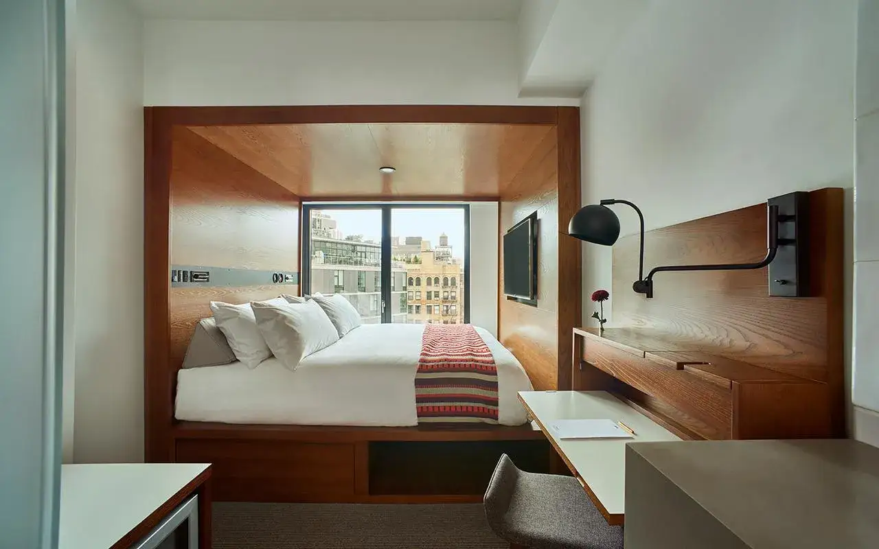 Mysig hotellrum inredning med säng, skrivbord och utsikt. Trädetaljer och modern design.
