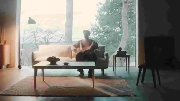 En person sitter i en soffa i ett rum med dansk design inredning. Ett stort fönster visar en vinterskog.