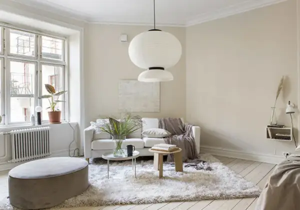 Ljust vardagsrum med en vit soffa, fluffig matta och en stor taklampa. Naturinredning med växter och trädetaljer skapar en lugn atmosfär.